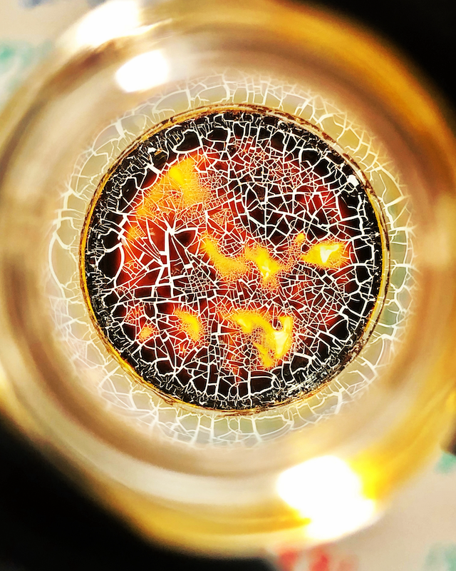An orange, yellow and black center resembling fire sitting inside a larger gold circle, with a random pattern of white cracks overlaying the center