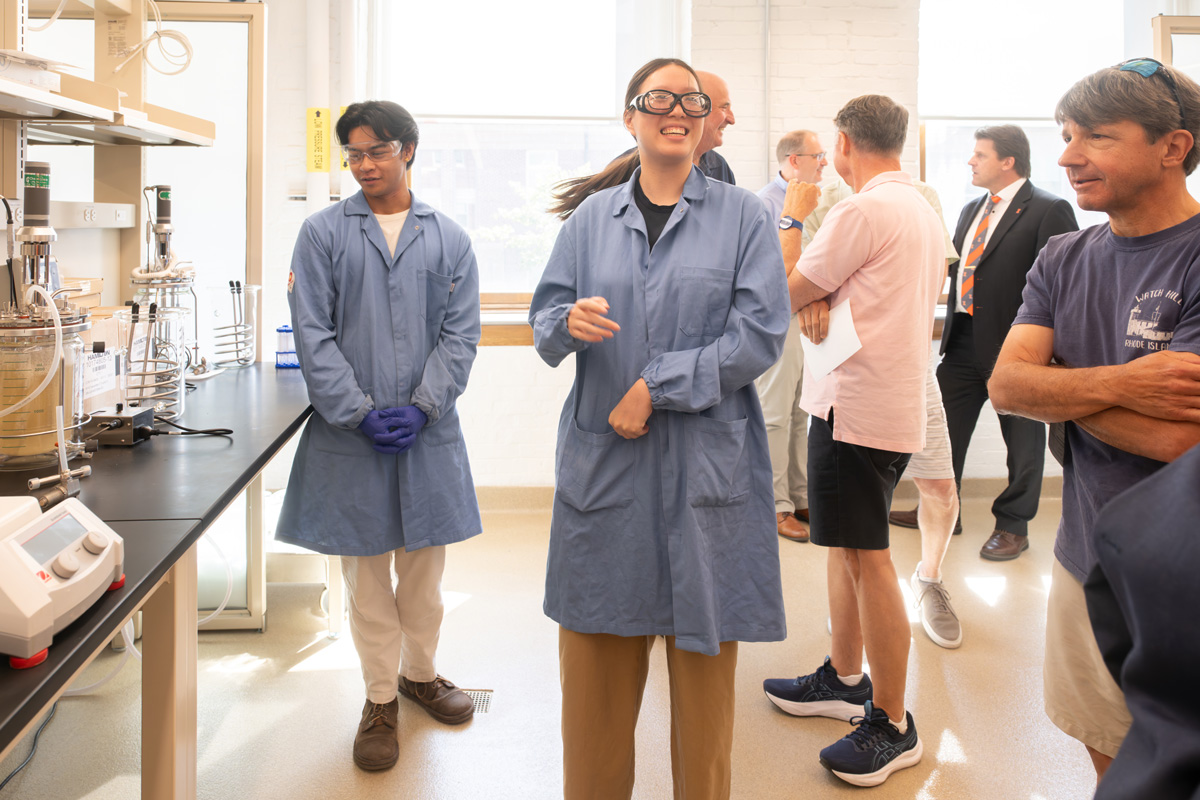 students in lab coats showing the experiments to visitors