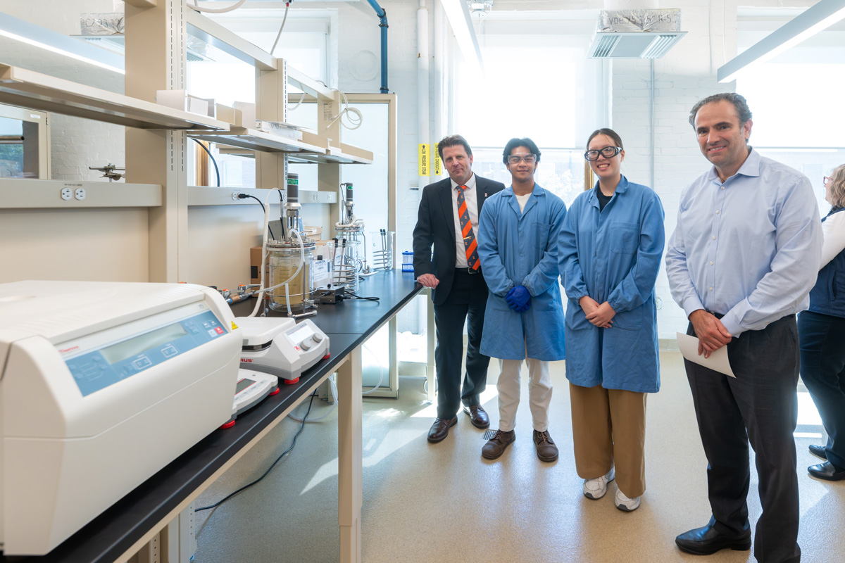 students in lab coats with lab visitors posing for the camera