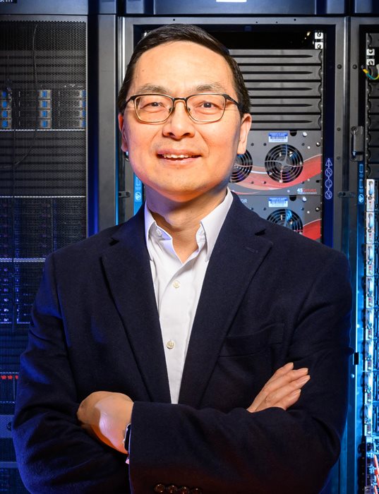 A man in a suit stands in front of a large supercomputer.
