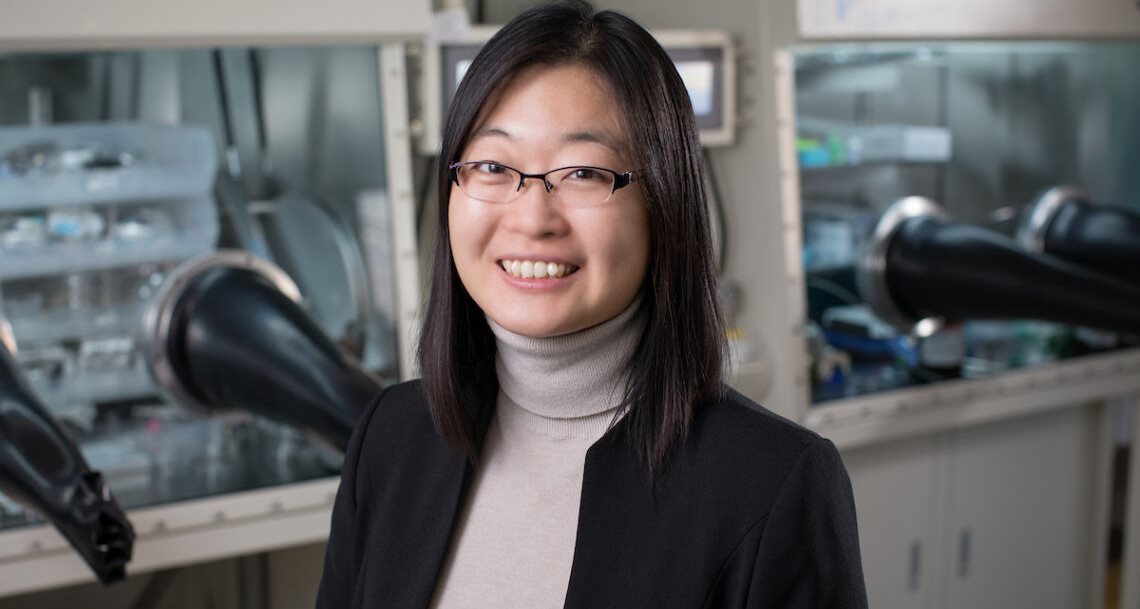 A woman with dark hair and wearing glasses, standing in front of laboratory equipment.
