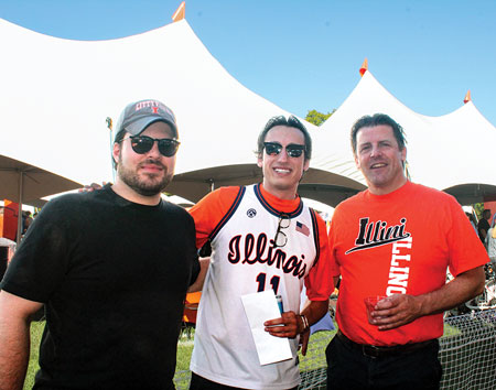 Three smiling men wearing Illini attire standing in front of a large white event tent.
