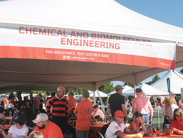 A crowd of alumni mingling under a large white tent.