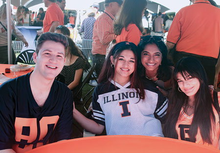 Four students wearing Illini attire having fun at the homecoming tailgate.