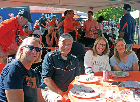 Alumni and guests wearing Illini attire mingling in the event tent