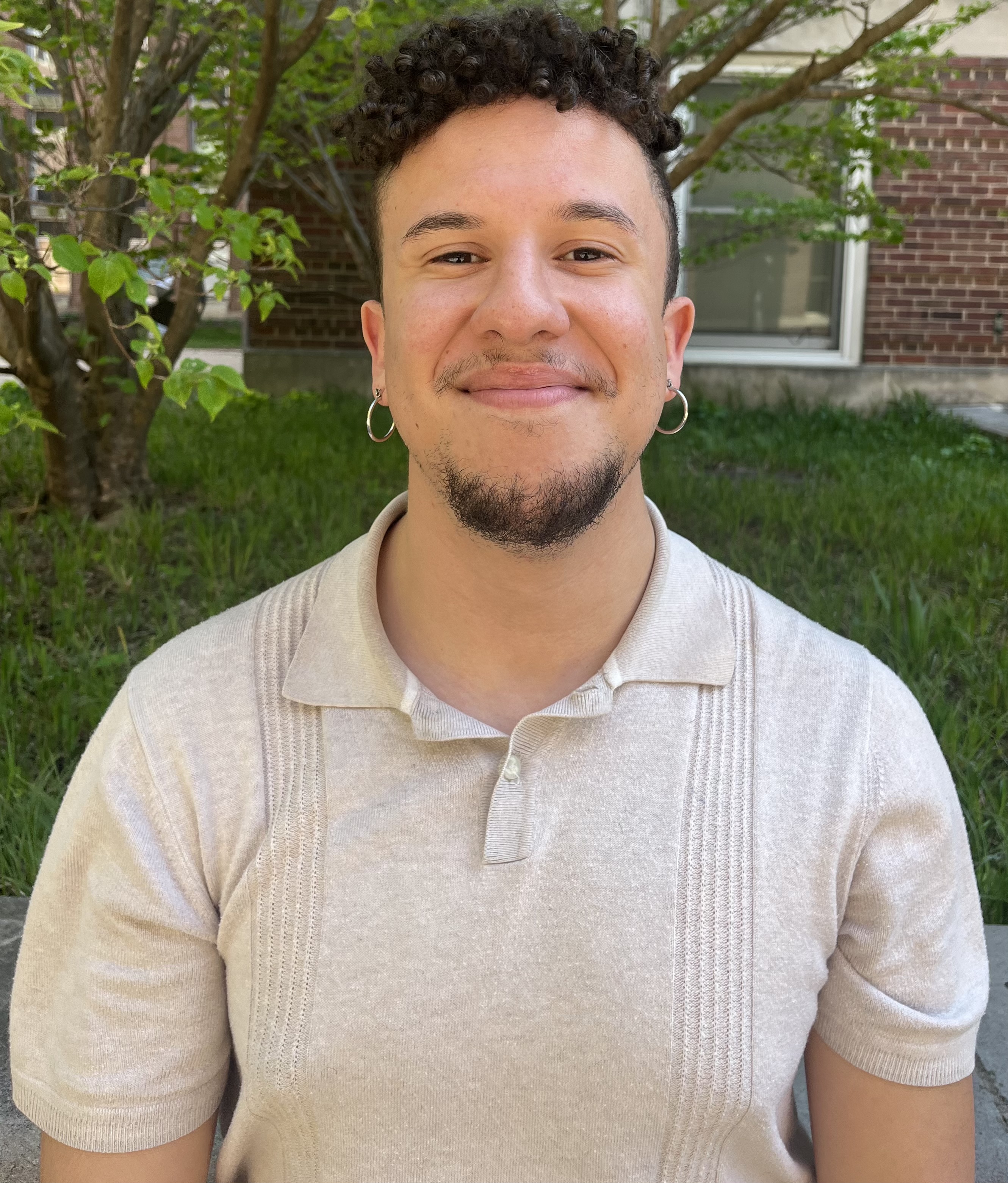 A young man wearing a tan colored polo smiles for a photo.