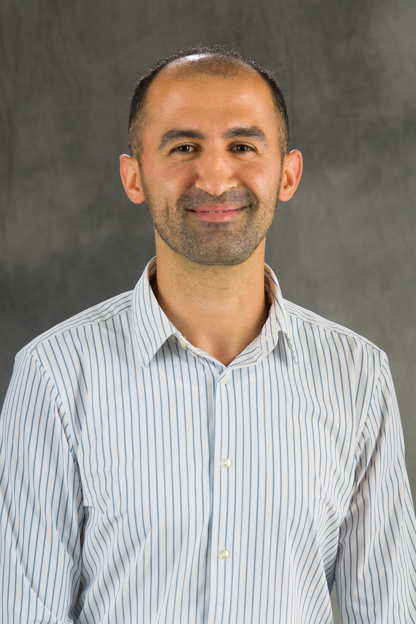 A man wearing a striped, button-down shirt smiles for a professional headshot.