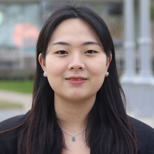 A young woman wearing a black suit jacket smiles for a professional photo.