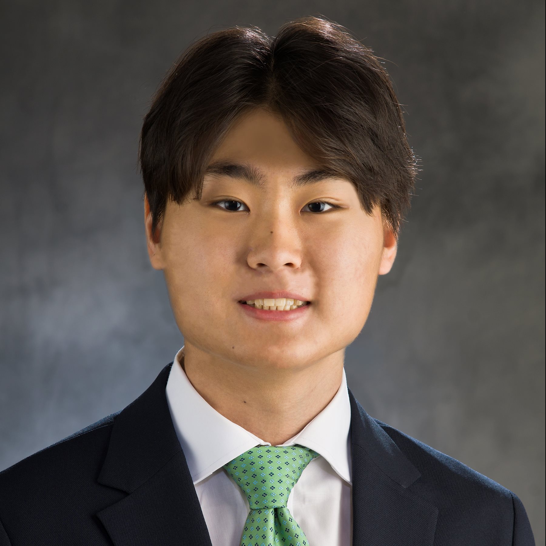 A young man wearing a suit jacket and green tie smiles for a professional headshot.