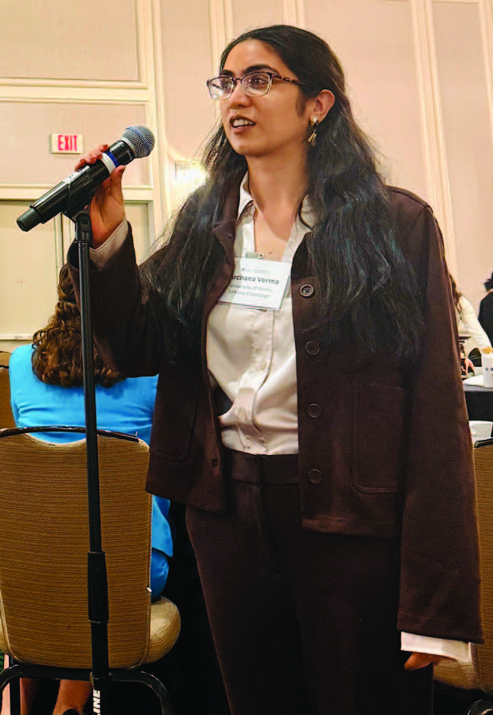 A young woman holds a microphone and prepares to raise a question to onlookers.