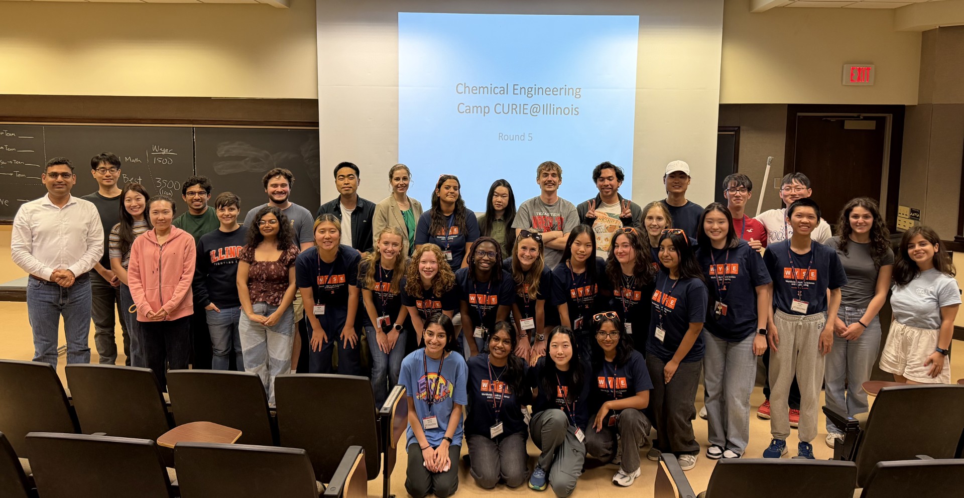 A group of students, faculty and campers gather for a group picture inside a lecture hall.