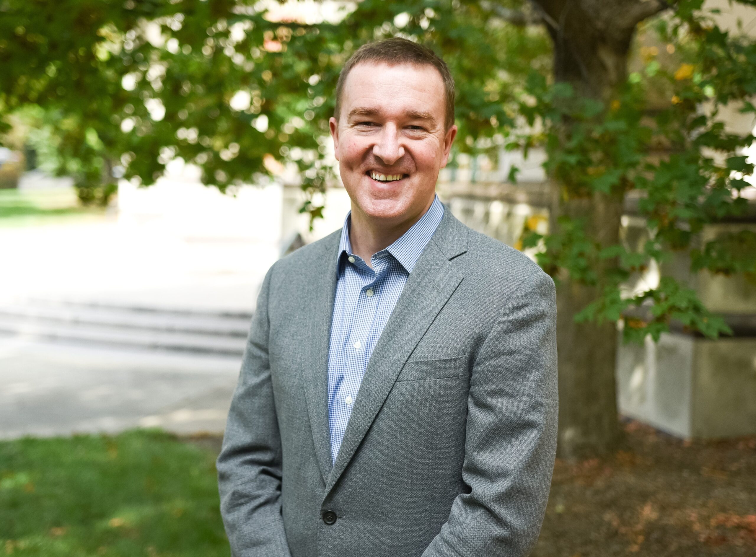 A man in a gray suit jacket smiles for a professional photo.