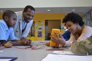 A student, Dr. Jerrod Henderson and Lonna Edwards measure the voltage of a potato battery.