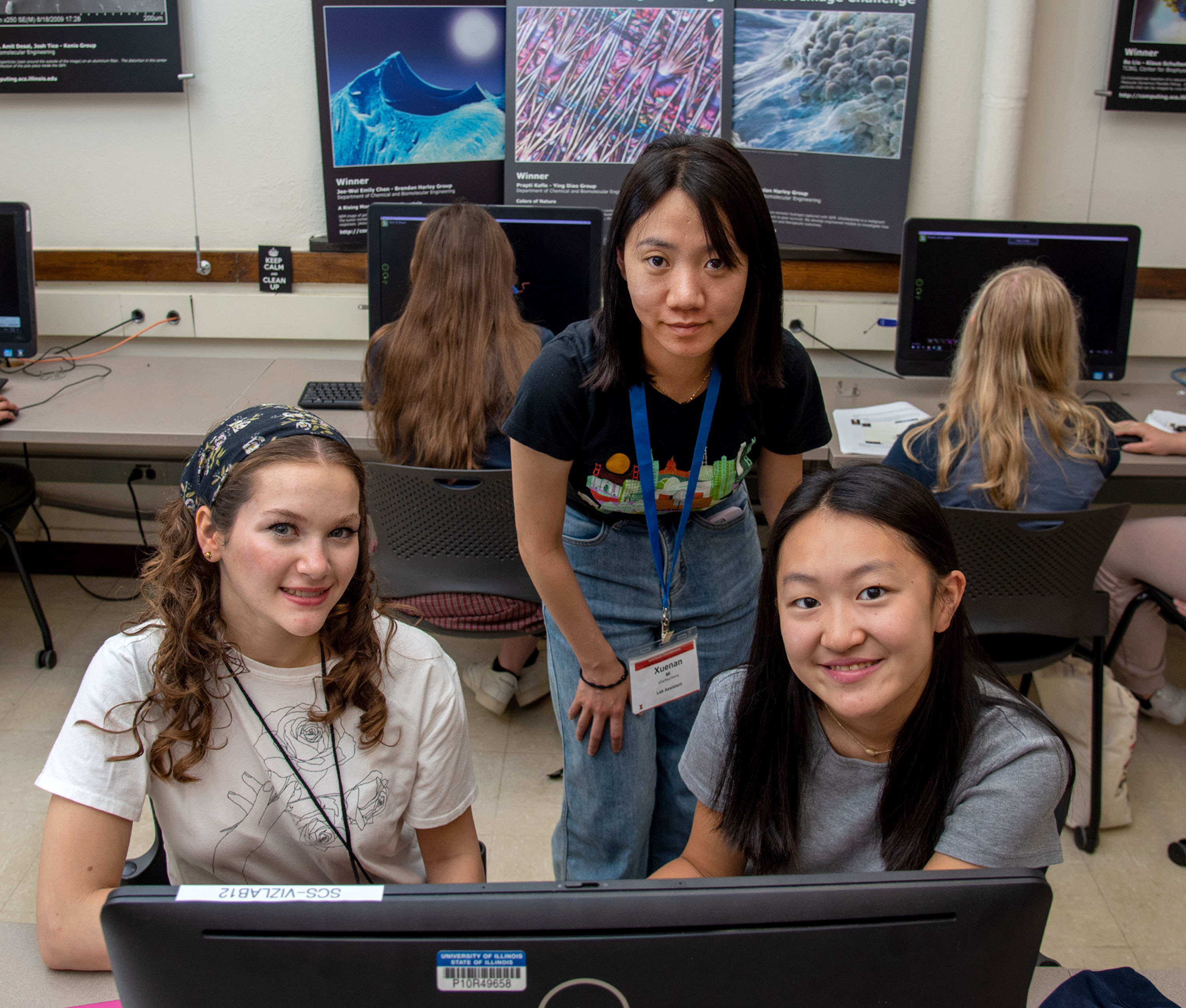 Three girls looking at the camera in a computer lab, one showing the other two how to do computer modeling