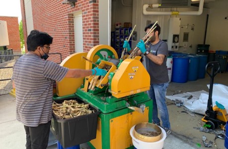 Above: Researchers Somesh Mishra and Narendra Deshavath press wild-type sugarcane for juice at the Integrated Bioprocessing Research Laboratory. Top: The Illinois research team in front of a fermenter at IBRL, from left: Jeremy Guest, Sarang Bhagwat, Jayne Allen, Somesh Mishra, Benjamin Crosly (back), Vijay Singh, Huimin Zhao, Shih-I Tan, Vinh G. Tran, and Saman Shafaei. Credit: CABBI Communications
