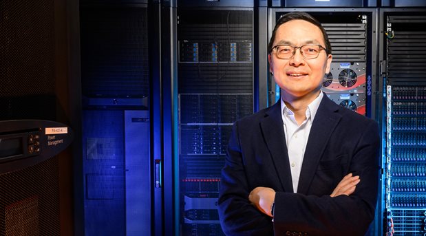 A man in a suit stands in front of a large supercomputer.